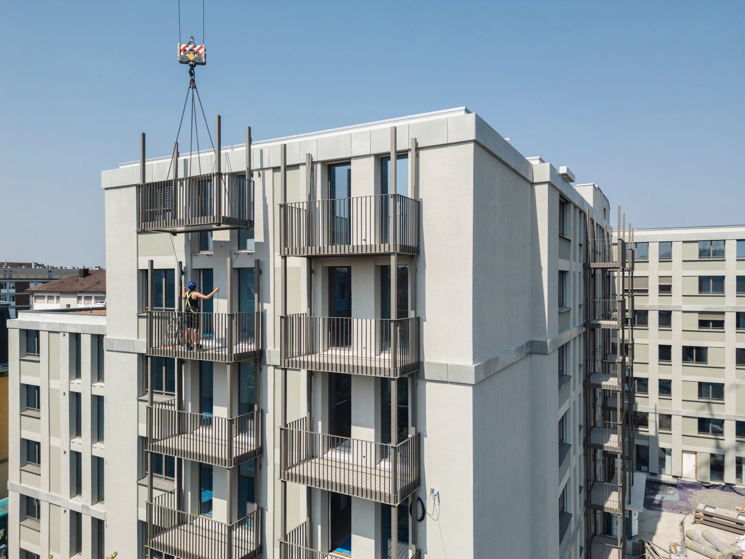 Neubau mit montierten Balkonen, ein Balkon hängt am Kran